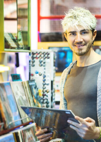 Young Man Choosing Vintage Vinyl LP In Records Shop Young Man Browsing Through Vintage Discs and Choosing Vinyl LP In Records Shop. Portrait of Customer Smiling At Camera And Buying Music Albums.