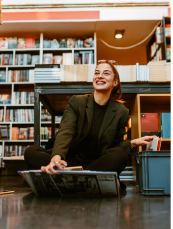 Portrait of smiling young brunette holding several vinyls while Portrait of smiling young brunette holding several vinyls while sitting on the floor at store. LPs gives whole different dimension to the music.
