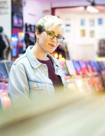 Young Woman Choosing Vintage Vinyl LP In Records Shop Young Woman Browsing Through Vintage Discs and Choosing Vinyl LP In Records Shop. Portrait of Customer Smiling At Camera And Buying Music Albums.
